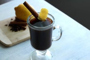 Coffee mug filled with a warming cocktail garnish with a cinnamon stick and lemon peel.