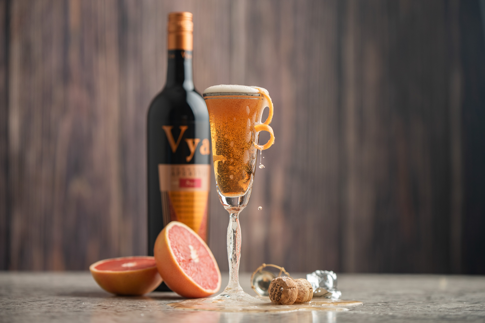 A champagne flute filled with the social hour cocktail with a bottle of Vya Sweet Vermouth in the background and grapefruit in the foreground.