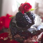 Flourless chocolate cake with blackberries and a rose bud on top.