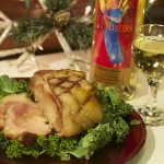 Sliced holiday ham on a plate next to a glass and bottle of Electra Moscato sweet wine surrounded by holiday decorations.