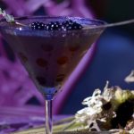 Purple poison cocktail in a martini glass with a lavender and blackberry garnish.