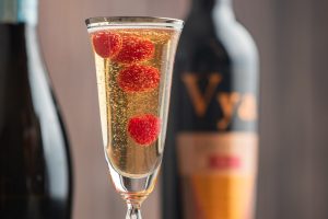 Closeup of a martini glass filled with socialite cocktail and raspberries in front of a bottle of Vya Sweet Vermouth and sparkling wine.
