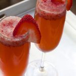 Two strawberry paradise royale cocktails in champagne flutes with strawberry garnishes.