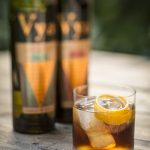 Vya half and half cocktail with ice and orange peel garnish next to bottles of Vya Extra Dry Vermouth and Vya Sweet Vermouth.