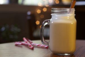 Egg nog mixed with Vya Sweet Vermouth in a glass mug on a table next to candy canes.