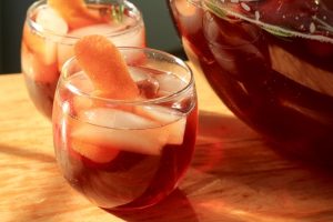 2 Perfect Port Punch cocktails in glasses filled with ice and grapefruit garnishes next to a bowl of more punch.