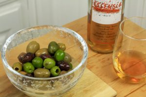Essensia marinated olives next to a glass and bottle of Essensia Orange Muscat dessert wine.