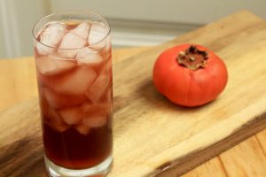 Ice filled Port Cobbler cocktail on a cutting board next to a persimmon.