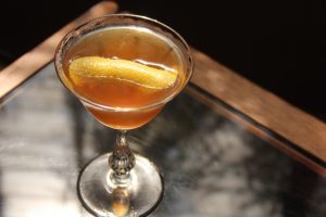 Wild tea cocktail in a glass with an orange peel garnish.