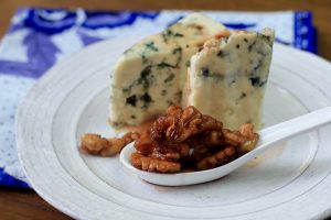 2 wedges of blue cheese next to a spoon of sugar glazed walnuts.