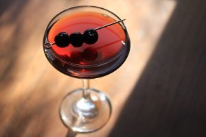Coupe glass with a dark liquor cocktail and maraschino cherry garnish.