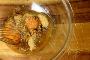 Bowl with whisk, raw egg and brown sugar inside.