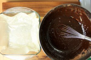 Bowl of melted chocolate next to a glass dish lined with parchment paper.