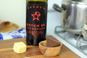 A bowl of chocolate, lump of butter and bottle of Starboard batch 88 port wine on a cutting board.