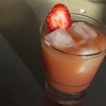 Strawberry paradise sunrise cocktail filled with ice and a strawberry garnish.