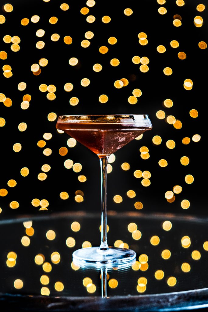 Midnight Manhattan on a mirrored table with twinkle lights in the background.