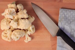 Chunks of cauliflower next to a knife on a cutting board.