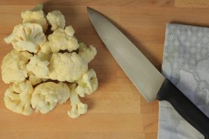 Chunks of cauliflower on a cutting board next to a knife.