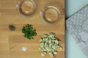 Pepper, blue cheese and green onion on a cutting board next to two small bowls.