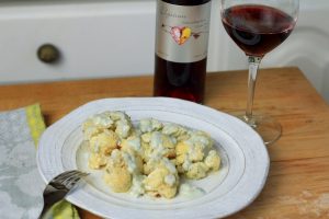 Dish with cauliflower covered in melted blue cheese next to a glass and bottle of Elysium Black Muscat dessert wine.