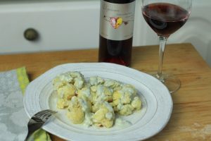 Roasted cauliflower and blue cheese dressing on a plate with a bottle and glass of Elysium Black Muscat dessert wine in the background.