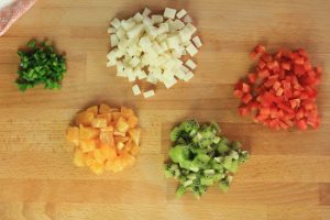 Diced up onion, pepper, tangerine and kiwi on a cutting board.