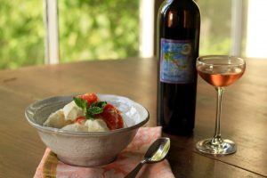 Bowl of ice cream, grapefruit puree and mint leaf next to a bottle and glass of Deviation dessert wine in front of a window.