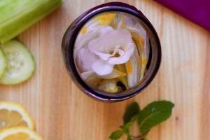 Looking inside a mason jar with edible flowers surrounded by lemons, mint and cucumber.