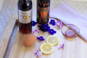 Elysium Black Muscat dessert wine and Vya Extra Dry Vermouth on a cutting board next to edible flowers, lemon wheels and an egg.