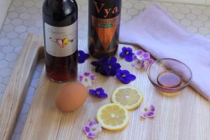 Elysium Black Muscat dessert wine and Vya Extra Dry Vermouth on a cutting board next to edible flowers, lemon wheels and an egg.