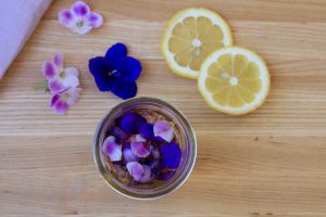 Looking inside mason jar filled with edible flowers with more edible flowers and lemon wheels around it.