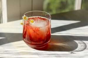 Low proof cocktail with a large ice cube and small edible flower garnish.