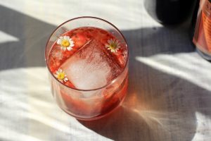 Low proof cocktail with a large ice cube and small edible flowers inside.