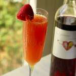 Mimosa cocktail in a champagne flute with a strawberry garnish in front of a bottle of Elysium Black Muscat dessert wine.
