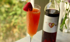 Mimosa cocktail in a champagne flute with a strawberry garnish in front of a bottle of Elysium Black Muscat dessert wine.