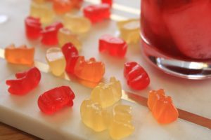 Gummy bears spread out next to the bottom of a Negroni cocktail.
