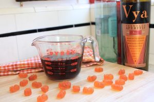 Gummy bears next to a measuring glass and a bottle of Vya Sweet Vermouth.
