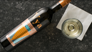 A bottle of Vya Whisper Dry Vermouth lying down next to a wine glass filled with vermouth.