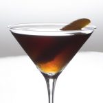 Manhattan cocktail with an orange peel garnish in a martini glass in front of a white background.