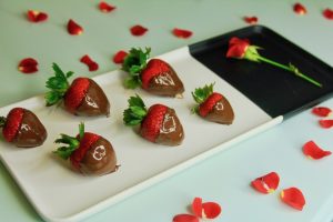 Chocolate covered strawberries made with Elysium Black Muscat Dessert wine for Valentine's Day on a dish surrounded by flower petals.