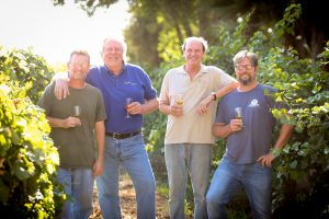 Winemakers Darin Peterson, Michael Blaylock, Andrew Quady and Herb Quady holding wine glasses in a vineyard.