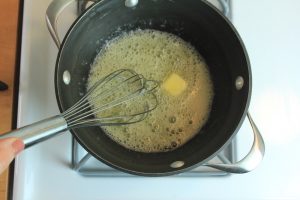 Butter simmering and being whisked in a pot on a stove.