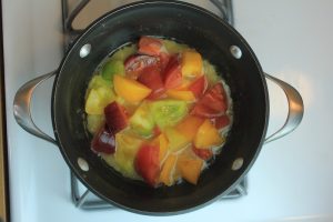 Peppers and tomatoes in a pot with butter on a stove.