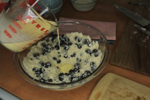 Pouring egg mixture into bowl with flour mixture and blueberries.