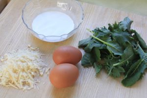 Bowl of cream with cheese, eggs and kale next to it.