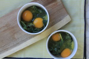 Two bowls with greens and raw eggs inside.
