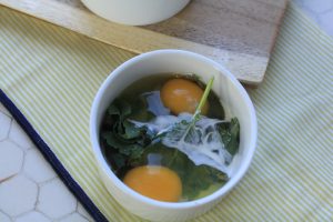 Bowl filled with greens, raw eggs and cream.