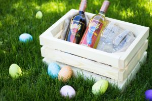 Wooden crate with a bottle of Electra Moscato, Red Electra Moscato and wine glasses inside on a bed of grass with Easter Eggs around it.
