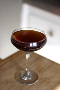 Port sherry and vermouth cocktail in a coupe glass on a table.