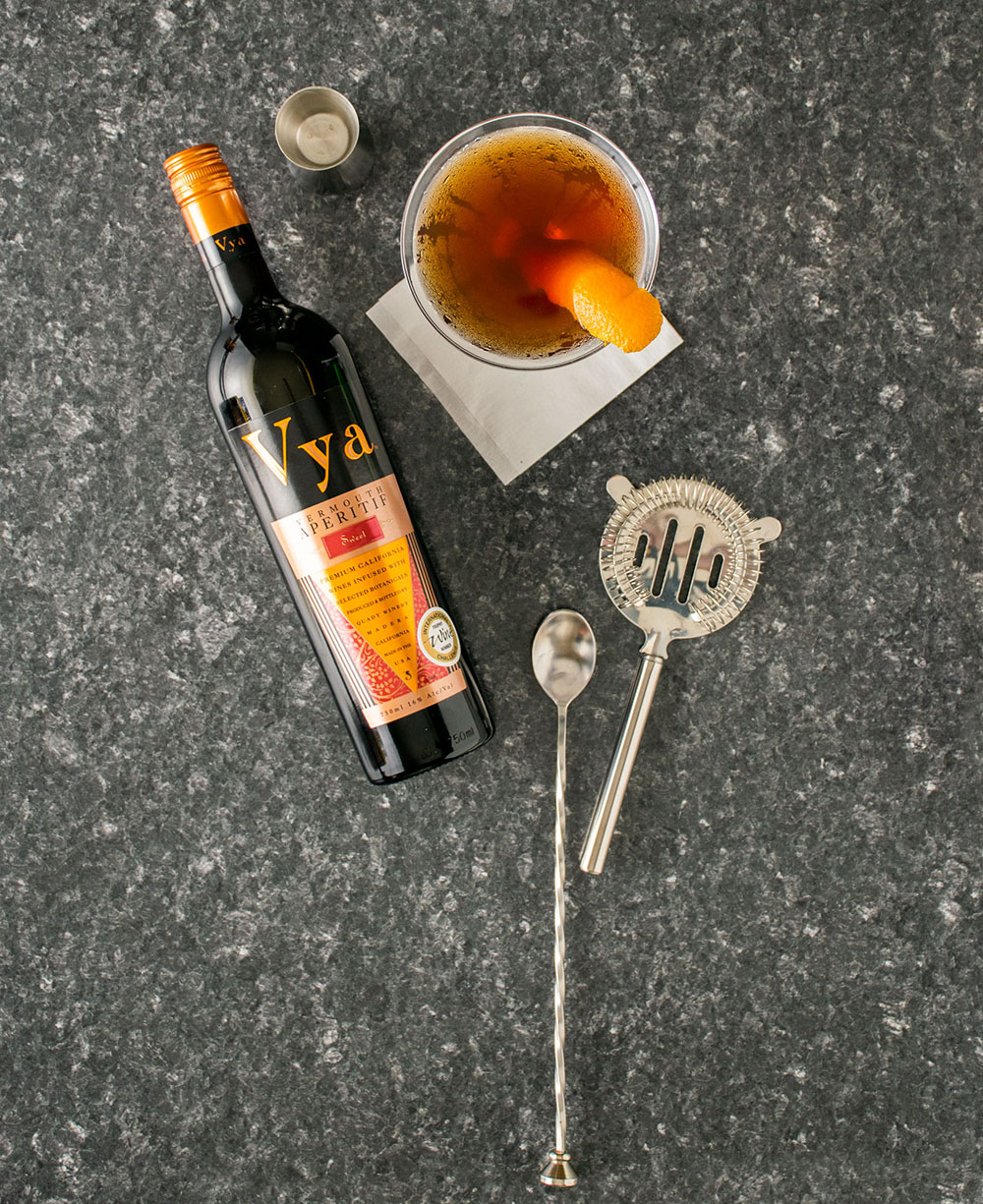Vya Sweet Vermouth bottle with a Manhattan cocktail garnished with an orange slice.